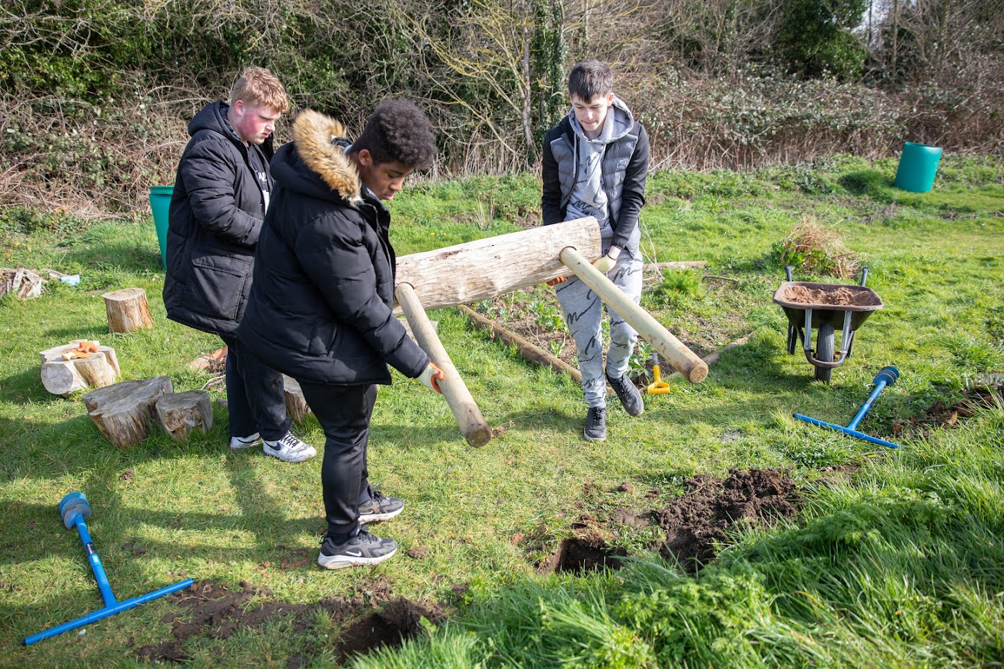 Group of 3 young people in a field. Two of them are carrying a bench, about to put it into pre-dug holes.