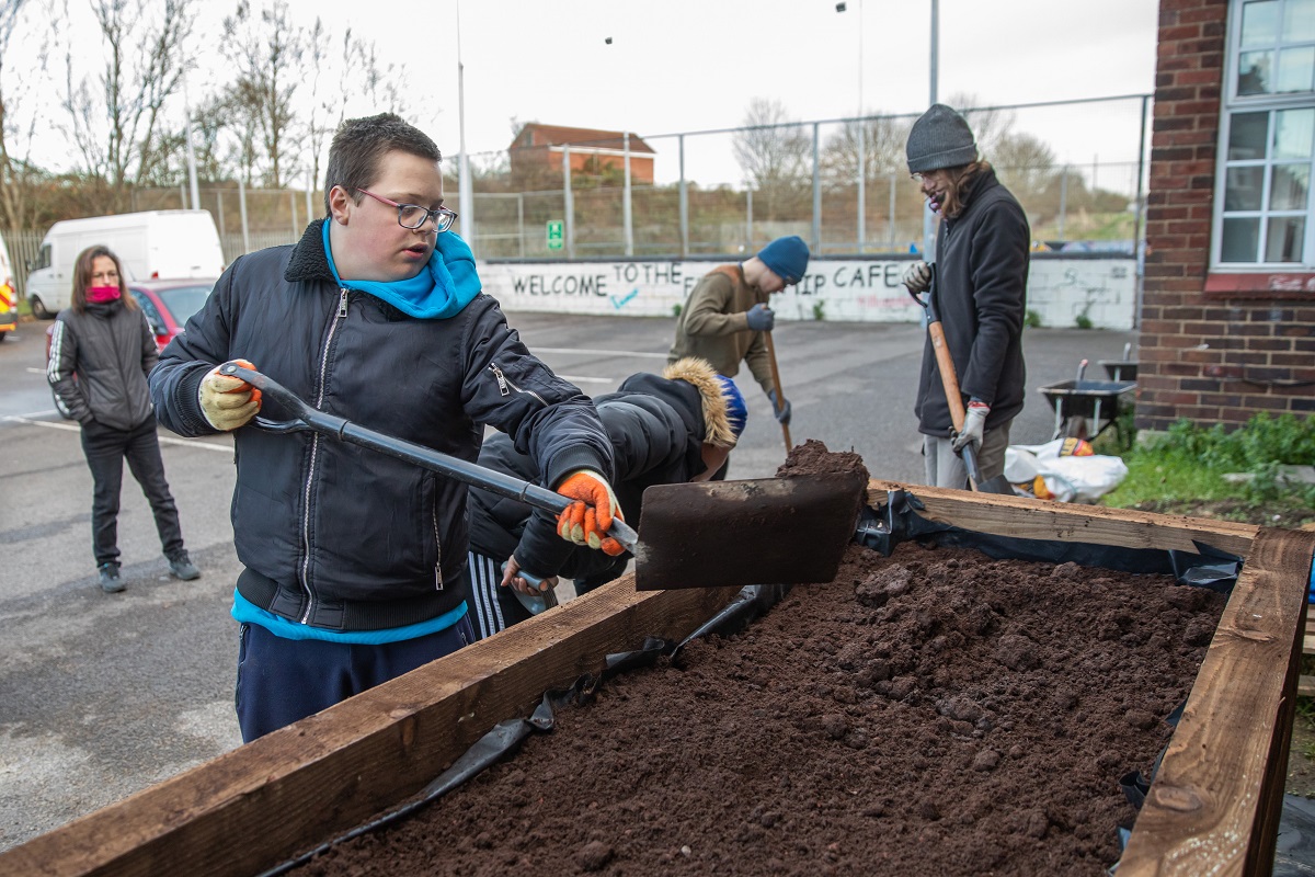 A young man using a shovel to add soil to a planter in The Friendship Cafe car park.