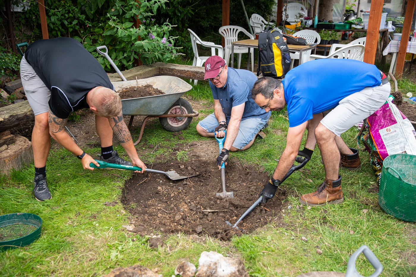 Three men using shovels to dig a hole for a fire pit.