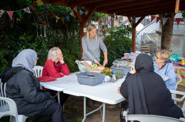 Rachel putting moss in a plant pot as she's watched by 4 sat-down women.