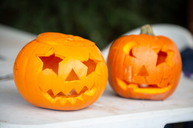 Two pumpkins on a plastic table. The one on the left has star eyes and the one on the left has one half-moon eye and one star eye.