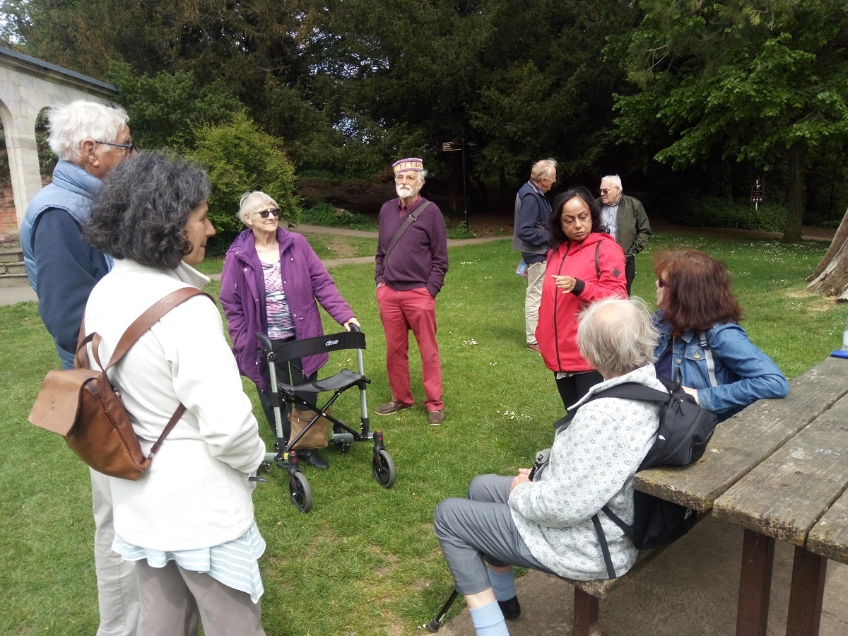 A group of 10 people, some sitting and some standing, talking with each other in a park.