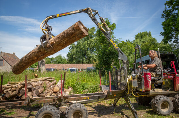 Gloucestershire Wildlife Trust employee in a mini crane lifting a wooden log up from a pile.