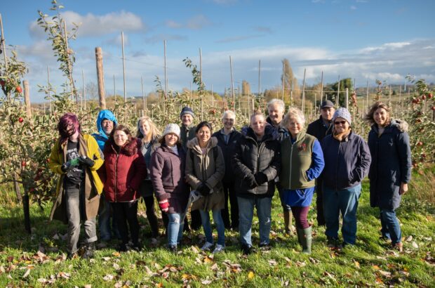 A group photo of everyone lined up in front of apple trees, smiling at the camera.