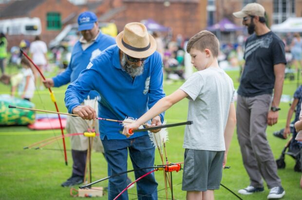 Archery instructor showing a young boy how to nock an arrow.