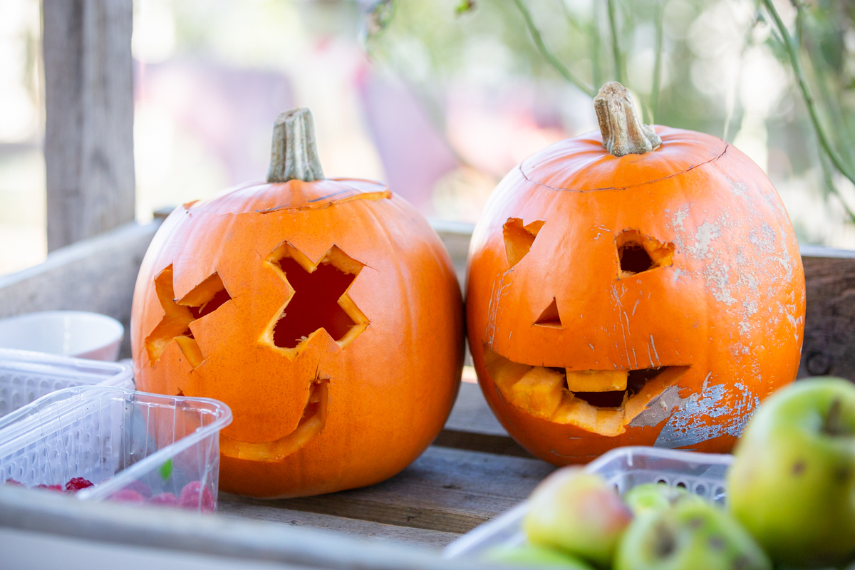 Two pumpkins on a shelf. The pumpkin on the left has crosses for eyes and a smiling face. The pumpkin on the right has hearts for eyes and a toothy smile.