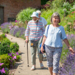 Three ladies walking along a path in the Museum in the Park's walled garden. The one at the front is smiling at the camera and touching some lavendar.