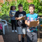 Three children walking down a path at our allotment, staring intently at their clipboards.