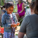 A girl smiling happily as she ties some light blue ribbon around a stick.