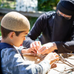 A lady helping her son to tie some wool around a stick.