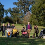 10 people standing and sitting, smiling at the camera with trees in the background.