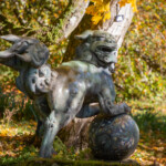 A statue of a Chinese Guardian Lion with yellow autumn leaves around it.