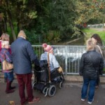 Group of people standing on a bridge and staring out over a river at Stratford Park.