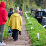 A line of people walking along Saul Junction, with water and narrowboats to the right of them,