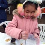 A child with a unicorn headband uses a spoon to mix fat and seeds together in a bowl at the allotment.