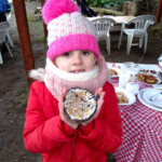 Child in a wooly hat holding half a coconut shell which has been filled with fat and seeds so it can be used as a bird feeder.