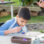 Child sat at a table focusing on painting their pebble red and blue.