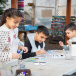 Group shot of three children painting pebbles at a table.