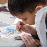 Close up of a child using a toothpick to paint a stone.