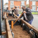 A man using a rake to level out the sand in a planter.