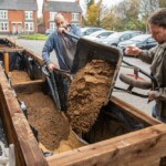 Two men tipping over a wheelbarrow full of sand into a planter.