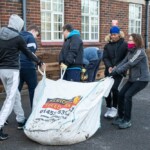 4 people dragging a bag full of soil toward some planters.