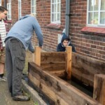Jon, the workshop manager, holding some wood in place as one young person watches and another drills the wood together to make a planter.