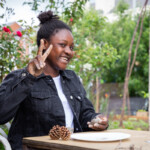 A young girl smiling and flashing the peace sign as she moulds some clay.