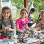 Three young girls sitting at a table, posing with a variety of clay statuettes.