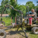 Gloucestershire Wildlife Trust employee in a mini crane about to lift a wooden log up from a pile.