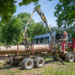 Gloucestershire Wildlife Trust employee in a mini crane using it to lay a wooden log on trailer.