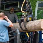 Close up of a crane arm lifting a wooden log into the back of the Fair Shares minibus.