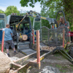 Gloucestershire Wildlife Trust employee in a minature crane lifting a wooden log into the back of the Fair Shares minibus.