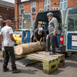 Half an ash log being pulled out from the back of the Fair Shares minibus by a team of 4 guys.