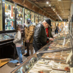 Group of people between two rows of exhibits, looking at items on either side.