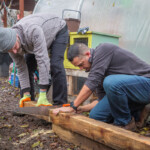 Two volunteers from Spirax Sarco using a saw to cut some wood into posts.