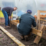 Two Spirax Sarco volunteers fixing the borders of plant beds. They're fixing a wooden plank to two posts.