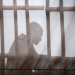 Actor behind a screen, showing a silhouette with bars symbolising a prison cell.