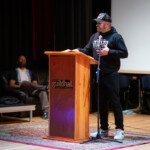 A wider shot of Mr. Milise reciting a spoken word poem with his hand on his chest.