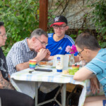 A group of people sat at a table at our allotment, eating burgers.