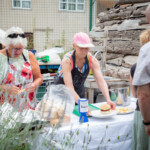 Viv handing over a plate with a burger on to a waiting lunch participant. Maureen is next to her preparing some cheese.