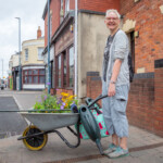 Kathy holding a wheelbarrow full of plants, smiling at the camera.
