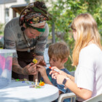 Young boy being helped to stick a flower to his fairy, as an older sibling watches.