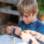 A young boy focusing as he plucks petals off a daisy to decorate his fairy.