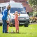 Young girl with one eye closed, taking aim at the target. The archery instructor is watching her along with another child.