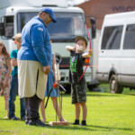Young boy holding the string on his bow back, about to let loose his arrow. Ashraf is watching him and three other kids are waiting in line.
