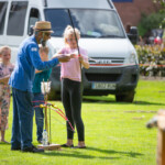 Archery instructor showing a young girl how to nock an arrow while two other kids wait in line.