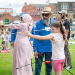 A young girl holding a bow and arrow, pulling the string back, moments before letting go.