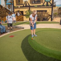 Group of participants playing outdoor crazy golf. Helen is about to putt the ball into the hole.