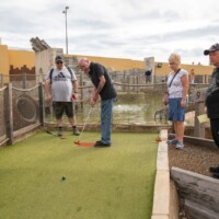 A group of participants playing outdoor crazy golf. Gary is hitting the ball.
